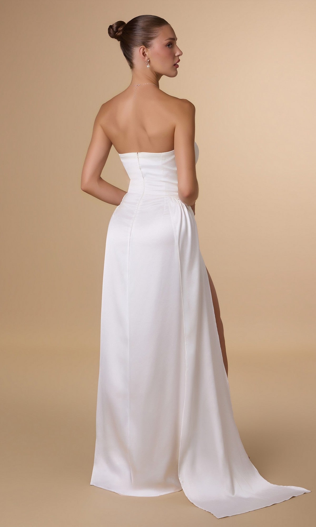 A woman with her hair in a bun faces away, modeling the Amoris T215W Strapless Long Satin Prom Dress with a high slit, set against a plain beige background—an elegant formal option under $150.